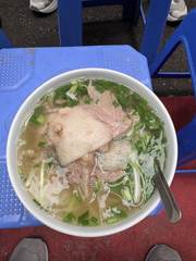 A bowl of pho on a blue plastic stool