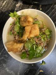 A bowl of soup topped with herbs and fried dough